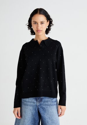 Pullover nero con collo a camicia, dotato di una chiusura con bottoni e piccole pietre preziose sparse. Texture morbida, vestibilità comoda, abbinato a jeans blu.
