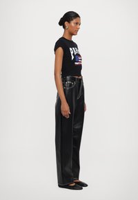 Black cropped t-shirt with "PARIS" and a flag design, paired with high-waisted black leather wide-leg pants. Flat black shoes complete the look.