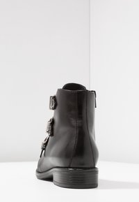 Černé kožené kotníkové boty s třemi kovovými přezkami, skromným podpatkem a hladkou texturou s zaoblenou špičkou a čistým šitím.