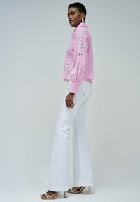 Chemise rayée rose et blanche avec broderies florales, assortie à un pantalon blanc évasé et des talons à lanières. Texture lisse, coupe ajustée.