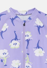 Une combinaison de bain zippée de couleur violet clair avec un motif floral en blanc et vert, agrémentée d'accents bleus. Tissu lisse avec des manches raglan.