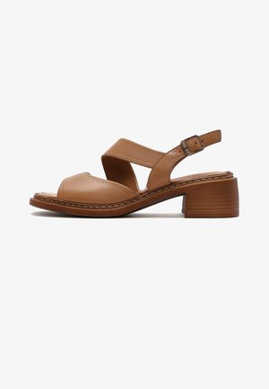 Sandale ouverte en cuir marron avec un petit talon carré, larges brides croisées et une boucle ajustable à la cheville.