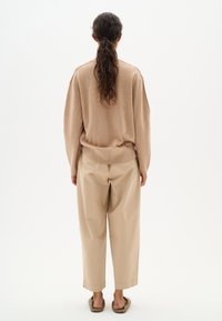 Maglione beige oversize con spalle scese, abbinato a pantaloni beige larghi. Tessuto liscio e design semplice, senza motivi o accenti visibili.