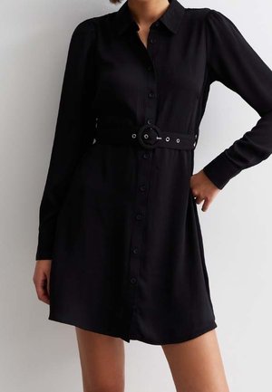 Czarna sukienka koszulowa z długim rękawem, zapinana na guziki z przodu, z bufkami na ramionach oraz pasem w talii z okrągłą klamrą.