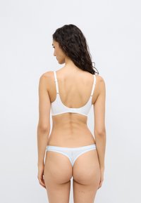 Λευκό ασύρματο σουτιέν με ρυθμιζόμενους ιμάντες και απαλό ύφασμα, συνδυασμένο με γαλάζιο στρινγκ με διακριτική λεπτομέρεια σχεδίου.