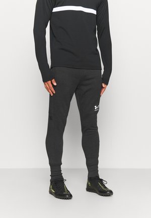 Sportowy strój składający się z czarnej koszulki z długim rękawem z białym paskiem oraz ciemnoszarych, zwężanych spodni dresowych z akcentami z logo i kieszeniami.