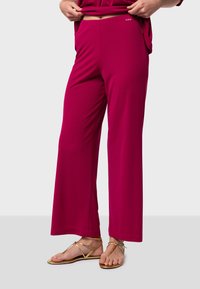Pantalons larges fuchsia en tissu doux, dotés d'une taille élastique et de poches. Associés à des sandales plates dorées pour un look décontracté.