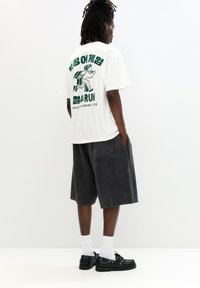 White t-shirt with green graphic on back depicting a runner and text. Paired with dark gray shorts and black shoes. White socks visible.