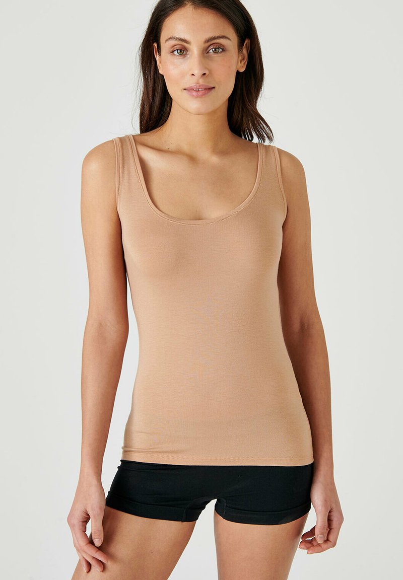 Beige tank top with a scoop neckline, made of lightweight fabric, featuring thin straps and a fitted design. Worn with black shorts.