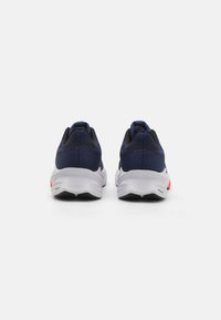 Chaussures de course avec une tige en maille bleu marine, une semelle de confort blanche et des accents rouges, présentant un design texturé et une silhouette basse.