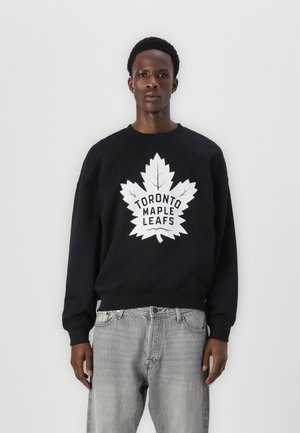Sweatshirt noir avec un grand logo blanc des Toronto Maple Leafs mettant en avant un design de feuille d'érable sur le devant. Le matériau semble doux avec des poignets côtelés.
