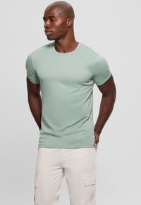 Camiseta de manga corta, con cuello redondo, en tejido verde claro, con un pequeño logo en el pecho y una textura suave.