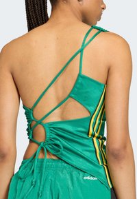 Zelený športový tielko s prekríženým dizajnom na chrbte, nastaviteľnými šnúrkami a žltými pruhmi; vyrobené z hladkého, lesklého materiálu.