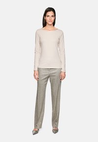 Beige Langarmshirt kombiniert mit grauen, gestreiften weit geschnittenen Hosen. Die Schuhe sind graue spitze Ballerinas. Einfaches Design mit lockerem Schnitt.