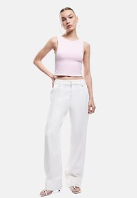 Lichtroze cropped tanktop met een gladde textuur, gecombineerd met hooggewaisted witte broek met voorplooien en een rechte snit.