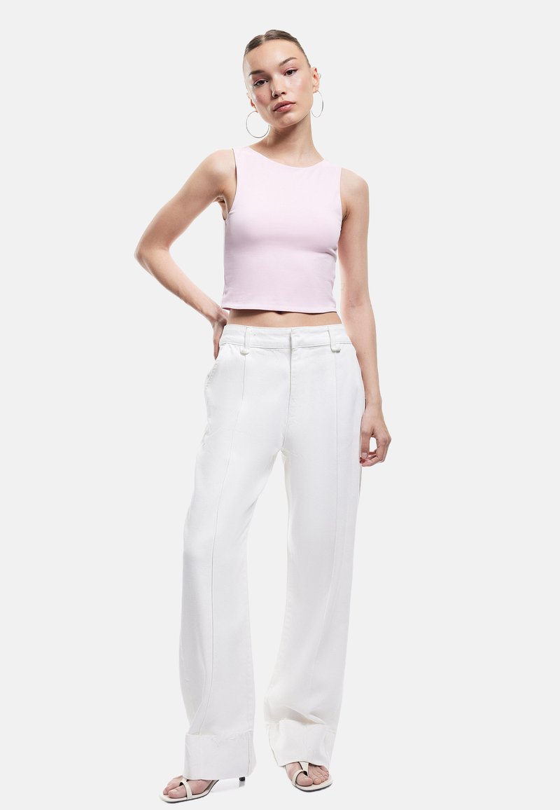 Lichtroze cropped tanktop met een gladde textuur, gecombineerd met hooggewaisted witte broek met voorplooien en een rechte snit.