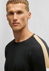 T-shirt noir avec un col rond et une bande beige sur l'épaule. Texture lisse et design ajusté.