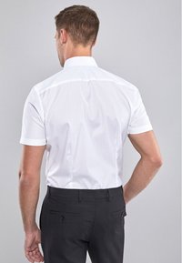 Witte shirt met korte mouwen, een klassieke kraag, een gladde textuur en een getailleerde pasvorm, in combinatie met donkergekleurde broeken met achterzakken.