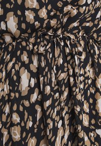 Svart tyg med leopardmönster i beige och krämfärg, med en rynkad midja och knytning. Mjuk textur med flödande veck.