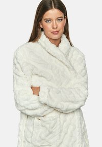 Witte pluche badjas met een textuur van golven, voorzien van een sjalkraag en lange mouwen. Inclusief een voorzak en gouden accenten.