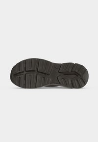 Semelle de chaussure en caoutchouc noir avec des rainures profondes et un motif texturé pour l'adhérence, vue de dessous sur fond blanc.
