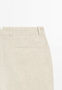 Beige rutiga byxor som visar bakre midjeband med bältesöglor och en enda horisontell slitsficka.
