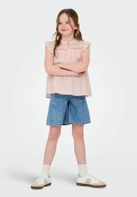 Ljusrosa, ärmlös topp med volangaxlar och vertikala r�änder; matchad med blekta denimshorts; vita sneakers med beige detaljer.