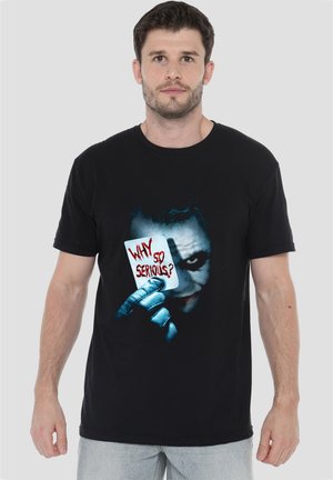 Man wearing a black t-shirt with a graphic of the Joker holding a card that reads "Why so serious?" in red letters.