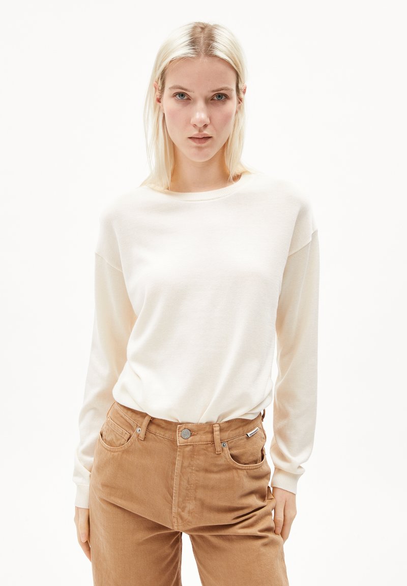 Light beige long-sleeve top made of soft fabric, featuring a round neckline and relaxed fit. Paired with light brown high-waisted pants.