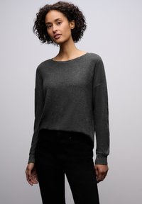 Tummanharmaa neule pehmeällä tekstuurilla, rento malli, leveä kaula-aukko ja pitkät hihat. Yhdistetty mustiin housuihin, joissa on hillittyjä yksityiskohtia.