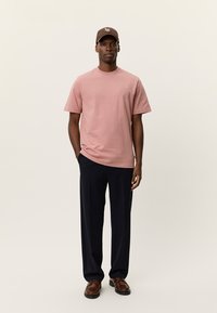 Ροζ ανοιχτόχρωμο κοντομάνικο μπλουζάκι με μινιμαλιστικό σχέδιο, σε συνδυασμό με σκούρο μπλε παντελόνι φαρδιάς γραμμής και καφέ παπούτσια με υφή.