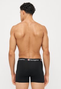 Black boxer briefs with a Champion logo waistband, featuring a snug fit, smooth texture, and minimalistic design. Positioned from the back.