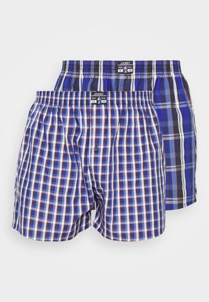 Twee paar herenboxers met een geruit patroon. Een paar is blauw met witte en rode accenten; het andere is donkerblauw met een lichtere ruit.