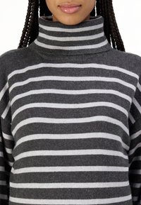 Un pull-over à col roulé rayé gris et blanc, fabriqué en tissu doux et texturé, avec un col haut et une coupe décontractée. Design casual avec des manches larges.