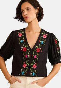Fekete blúz puffos ujjakkal, mély V-kivágással és színes rózsaszín és kék virágmintázattal. Textúrált anyag gombos díszítéssel.