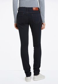 Mörkblå skinny jeans med medelhög midja, bakfickor och en brun läderlogotyp. Bärs med en randig långärmad topp.