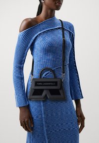 Black leather shoulder bag with a structured design, featuring a top handle, adjustable strap, and logo detailing on the front.