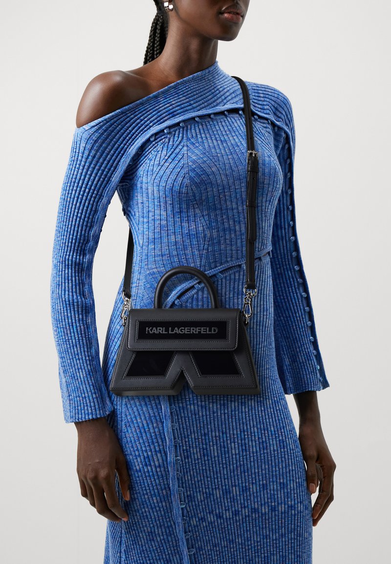 Black leather shoulder bag with a structured design, featuring a top handle, adjustable strap, and logo detailing on the front.