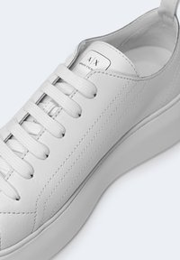 Baskets en cuir blanches Armani Exchange avec des lacets blancs, des coutures visibles et le logo sur la languette, vues sous un angle supérieur latéral.