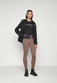 Czarna kurtka o dopasowanym kroju, czarna koszulka z logo Terrex, brązowe legginsy i czarne trampki. Posiada małą czarną kieszonkę z przodu.