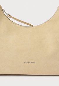 Borsa in camoscio beige con una texture liscia, forma semicircolare e dettaglio logo in tonalità argento. Presenta una cerniera e un accento in pelle.