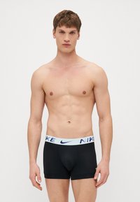 Crne bokserice s laganim plavim pojasom na kojem piše "NIKE". Tkanina izgleda rastezljivo i glatko, namijenjena udobnosti i prilagodbi.