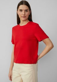 Rode t-shirt met korte mouwen van zachte stof, met een ronde hals en een getailleerde pasvorm, gecombineerd met lichte broeken.