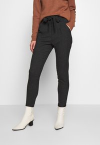 Dark gray tailored pants with a fabric texture, featuring a drawstring waist, side pockets, and a slim fit, paired with white ankle boots.