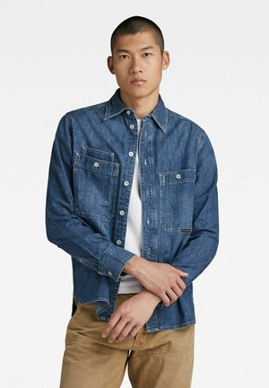 Denim shirt with a button-down collar, two chest pockets, and a light wash. Long sleeves, relaxed fit, and visible stitching details.
