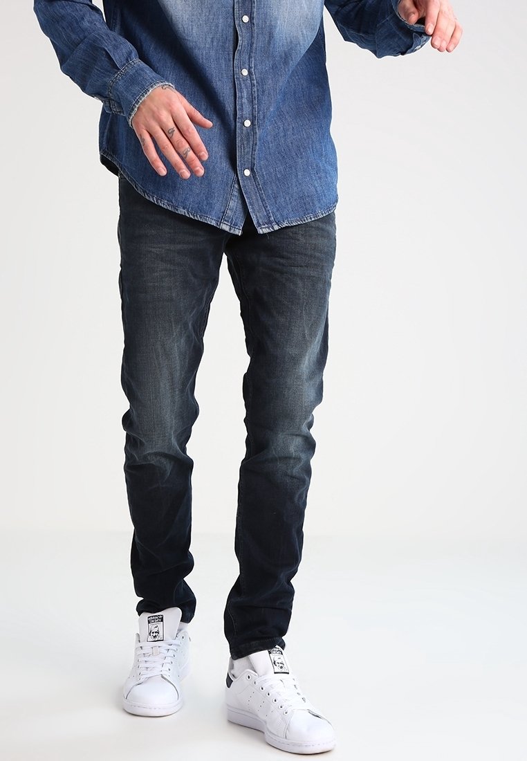 Camisa de denim en degradado azul, estilo de botones, combinada con jeans oscuros y zapatillas blancas. Diseño simple sin patrones o acentos visibles.
