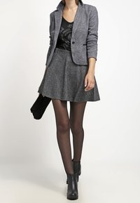 Grijze blazer met notch-lapels, fitted ontwerp. Zwarte graphic tanktop eronder. Grijze uitlopende rok, zwarte tights en enkellaarsjes. Zwarte clutch.