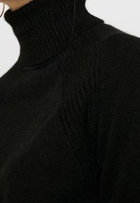 Černý rolák z měkké pleteniny s žebrovanou strukturou a přiléhavým střihem kolem límce a ramen.