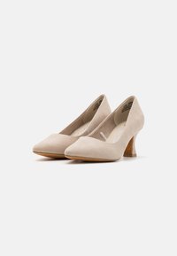 Escarpins en daim beige avec un bout pointu, un talon courbé et un détail en découpe sur les côtés. Texture lisse et design élégant.