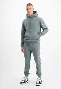 Lichtgroene hoodie met voorzak en trekkoord, gecombineerd met bijpassende trainingsbroeken met zijzakken en logo-accenten. Draag het met zwart-witte sneakers.